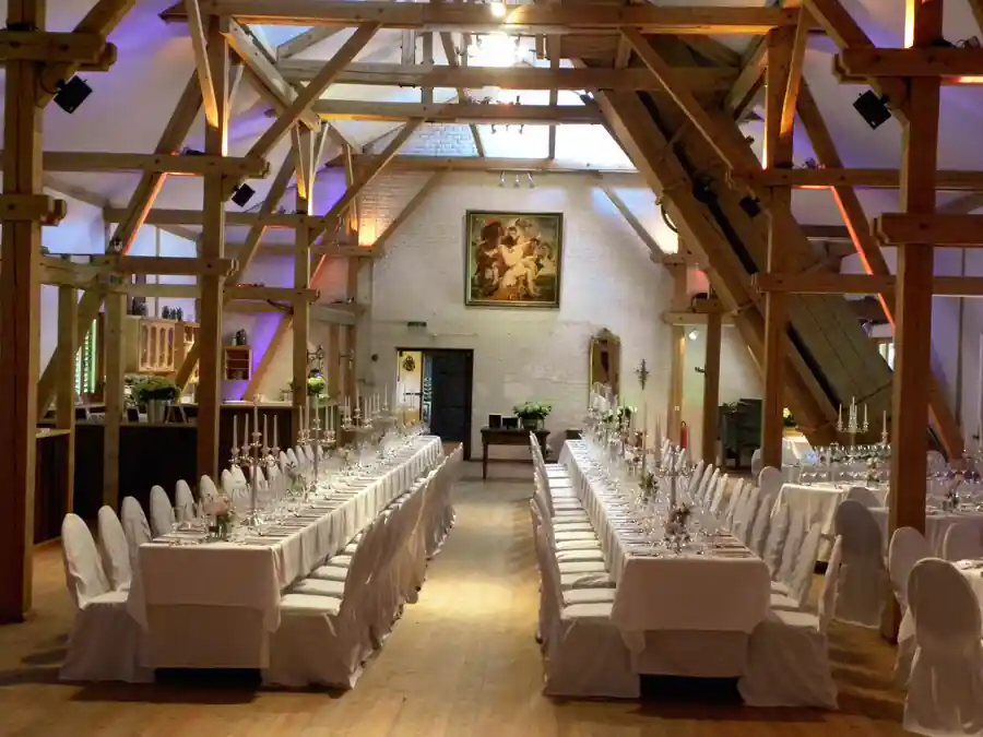 Saal, welcher weiß dekoriert ist und Holz an der Decke in brauner Holzfarbe beleuchtet in Lilalicht. Der Saal ist für eine Hochzeit mit der Band für Hochzeit in Glonn dekoriert. Wir sind deine Hochzeitsband Glonn in Bayern und in der Nähe von München.